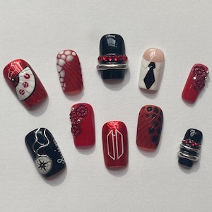 May include: A collection of ten artificial nails with various designs. The nails feature a range of colors, including red, black, and nude. Designs include patterns, embellishments, and a miniature tie.