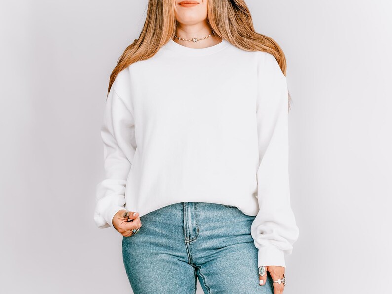 K&ouml;nnte beinhalten: Ein wei&szlig;es Sweatshirt mit Rundhalsausschnitt und langen &Auml;rmeln. Das Sweatshirt wird mit hellblauen Jeans kombiniert. Das Model tr&auml;gt eine Halskette und Ringe. Der Hintergrund ist eine schlichte wei&szlig;e Wand.