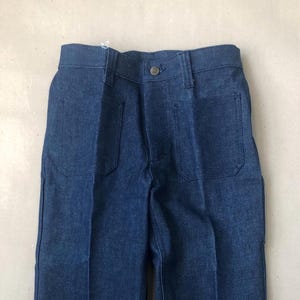 May include: A pair of blue denim pants with two front pockets and a button closure. The pants are made of a sturdy denim fabric and have a classic, straight-leg design. The pants are folded neatly, showcasing the details of the pockets and the button.