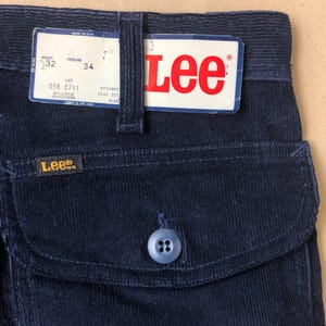 May include: Close-up of navy blue corduroy trousers with a back pocket and a button closure. The trousers have a tag that reads "Lee" in red and white. The waist size is 81 cm and the inseam is 86 cm.