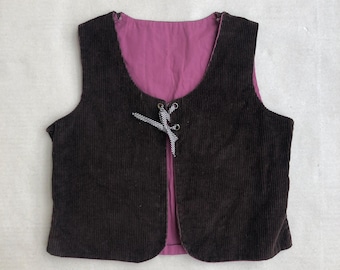 Op de afbeelding: Een bruin corduroy vest met een roze voering en een zwart-witte vetersluiting.