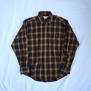 May include: A long-sleeved, button-down shirt in a brown and tan plaid pattern. The shirt features a button-down collar, a single chest pocket, and buttoned cuffs. The fabric appears to be a soft, flannel-like material.