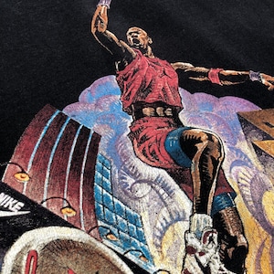 Może przedstawiać: Czarny T-shirt z nadrukiem graficznym koszykarza w powietrzu, ubranym w czerwoną koszulkę i białe buty sportowe, z widocznym napisem "NIKE" w lewym dolnym rogu koszulki.