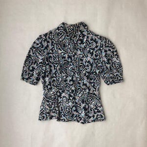 May include: A black and white paisley print blouse with a ruffled collar and short sleeves.