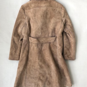 Puede incluir: Un abrigo de ante marr&oacute;n con cuello de piel sint&eacute;tica y cintur&oacute;n. El abrigo tiene una silueta larga y ajustada y un dise&ntilde;o cl&aacute;sico.