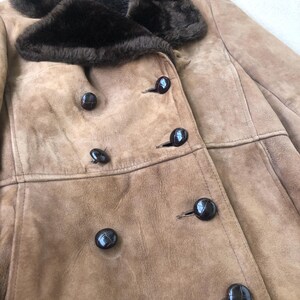Puede incluir: Una chaqueta de ante marr&oacute;n con cuello de piel sint&eacute;tica marr&oacute;n y varios botones negros. La chaqueta tiene cierre de doble botonadura.