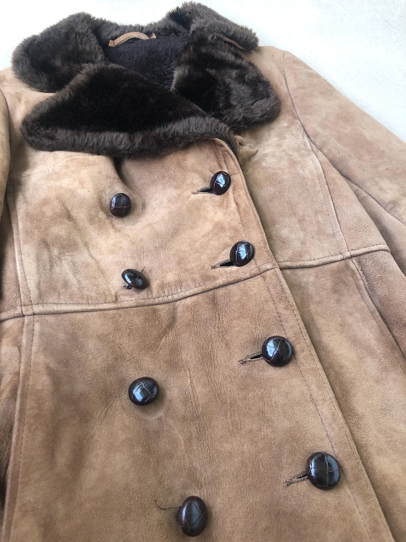 Puede incluir: Una chaqueta de ante marr&oacute;n con cuello de piel sint&eacute;tica marr&oacute;n y varios botones negros. La chaqueta tiene cierre de doble botonadura.