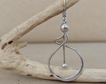 May include: A single silver earring with a unique, abstract design. The earring features a curved, open circle shape with a small ball at the bottom and a larger ball at the top, connected by a straight line. The earring hangs from a hook.