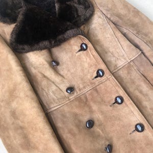 Puede incluir: Una chaqueta de ante marr&oacute;n con cuello de piel sint&eacute;tica marr&oacute;n y cierre de doble botonadura con botones marr&oacute;n oscuro.