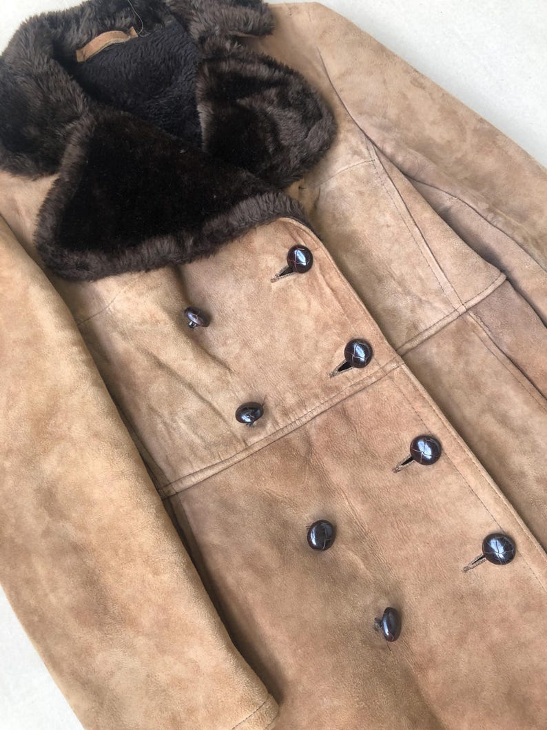 Puede incluir: Una chaqueta de ante marr&oacute;n con cuello de piel sint&eacute;tica marr&oacute;n y cierre de doble botonadura con botones marr&oacute;n oscuro.
