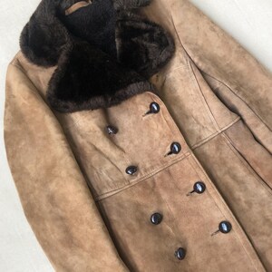 Puede incluir: Una chaqueta de ante marr&oacute;n con un gran cuello de piel sint&eacute;tica marr&oacute;n y cierre de doble botonadura con botones negros.