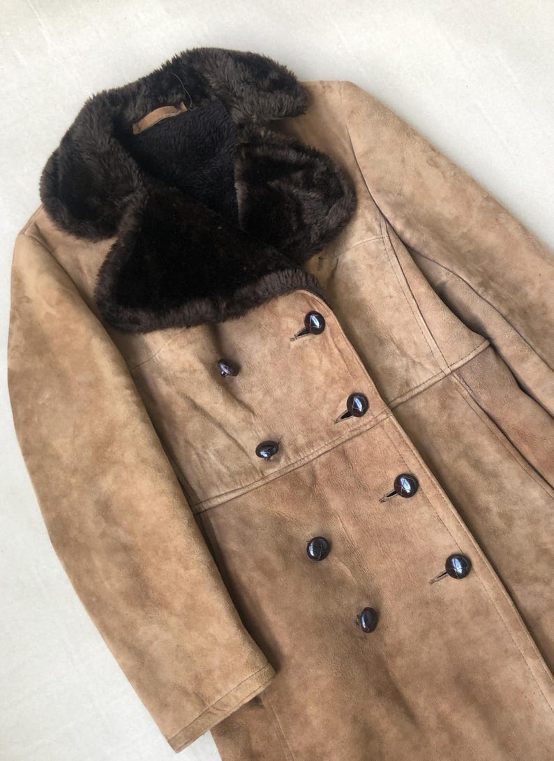 Puede incluir: Una chaqueta de ante marr&oacute;n con un gran cuello de piel sint&eacute;tica marr&oacute;n y cierre de doble botonadura con botones negros.