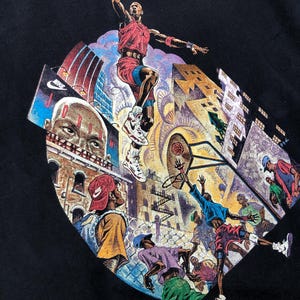 Może przedstawiać: Czarny T-shirt z nadrukiem graficznym koszykarza w czerwono-białej koszulce, skaczącego do wsadu. Grafika przedstawia r&oacute;wnież panoramę miasta z budynkami i koszem do koszyk&oacute;wki.