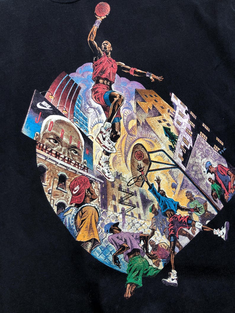 Może przedstawiać: Czarny T-shirt z nadrukiem graficznym koszykarza w czerwono-białej koszulce, skaczącego do wsadu. Grafika przedstawia r&oacute;wnież panoramę miasta z budynkami i koszem do koszyk&oacute;wki.