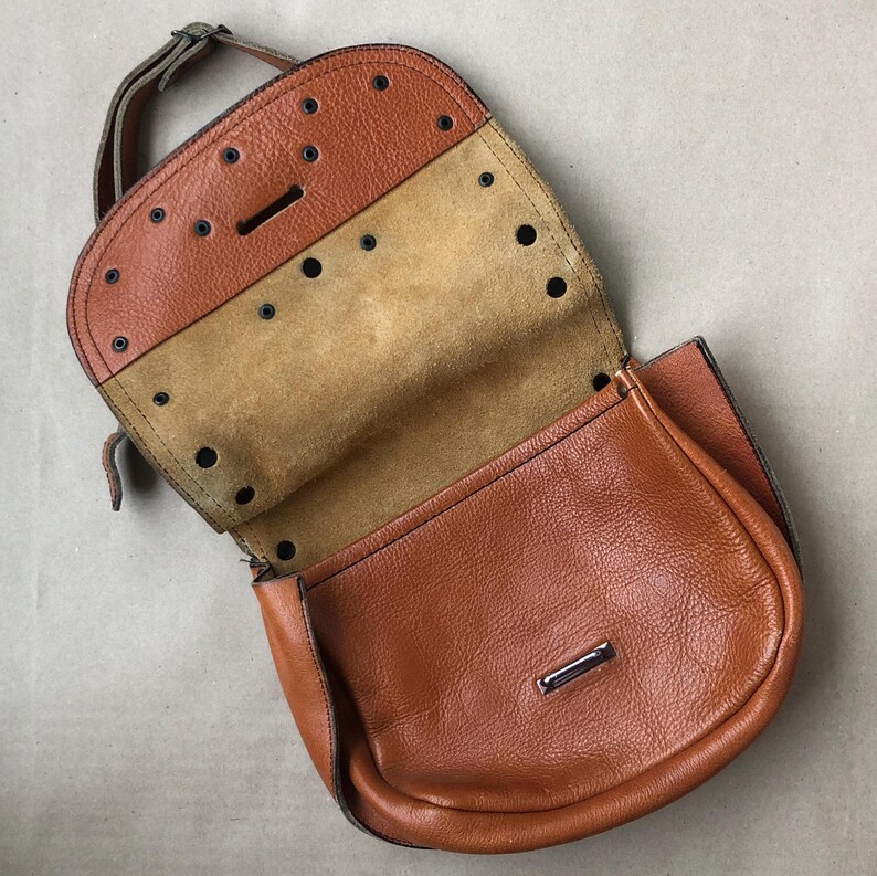 May include: A brown leather satchel bag with a flap closure and a metal buckle. The bag has a suede lining and a brown leather strap.