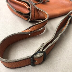 May include: A brown leather crossbody bag with a strap that has a buckle closure. The strap is adjustable and has a light brown trim.