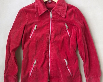 Puede incluir: Una chaqueta de pana de color rojo brillante con una cremallera frontal plateada de longitud completa, un cuello puntiagudo y cuatro bolsillos diagonales con cremallera en la parte delantera. La chaqueta tiene mangas largas con puños.