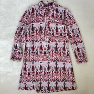 May include: A long-sleeved dress with a button-up collar and a geometric pattern in shades of red, black, and white on a gray background.
