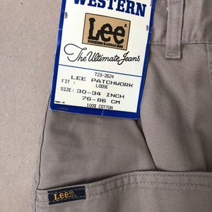May include: Close-up of tan Lee Patchwork jeans with a tag. The tag reads "WESTERN Lee The Ultimate Jeans" and lists the size as 30-34 inches (76-86 cm). The jeans are 100% cotton.