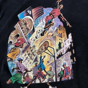 Może przedstawiać: Czarny T-shirt z kolorowym nadrukiem graficznym przedstawiającym koszykarzy w miejskim otoczeniu. Grafika przedstawia koszykarza w powietrzu, kosz do koszyk&oacute;wki i innych graczy na boisku. Grafika zawiera r&oacute;wnież budynki i inne elementy miejskie.