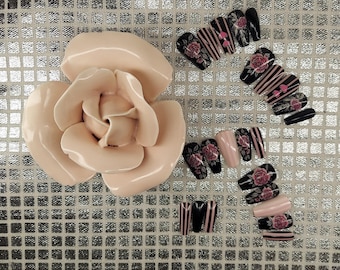 May include: A collection of artificial nails with various designs, including black nails with pink rose and stripe patterns, and solid pink nails. A large, light pink ceramic rose is also present.