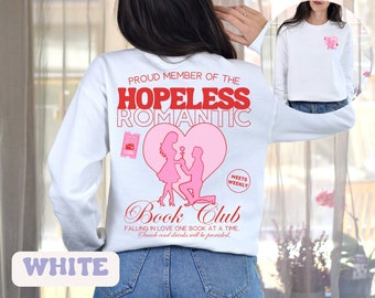 Könnte beinhalten: Weißer Langarm-Pullover mit einem rosa Herz-Motiv und dem Text "Proud Member of the Hopeless Romantic Book Club" in Rot. Die Grafik zeigt ein Paar in einem Herzen mit dem Text "Meets Weekly" und "Falling in Love One Book at a Time. Snack and drinks will be provided."