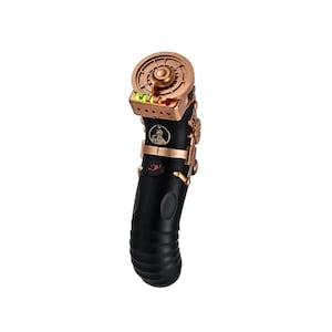May include: A black handheld device with a curved, ribbed grip and a copper-coloured top section. The top features a circular dial, a small rectangular display with green and red lights, and a circular emblem depicting a person. A red light is visible.