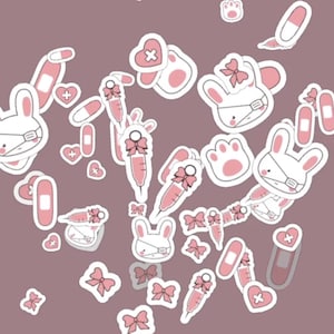 May include: A selection of white and pink stickers with a medical theme. The stickers feature bunnies wearing masks, syringes, bandages, hearts with crosses, and paw prints, all in a kawaii style. The background is a muted mauve colour.