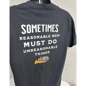 May include: Black t-shirt with white text that reads "Sometimes reasonable men must do unreasonable things". A yellow bulldozer is pictured below the text.