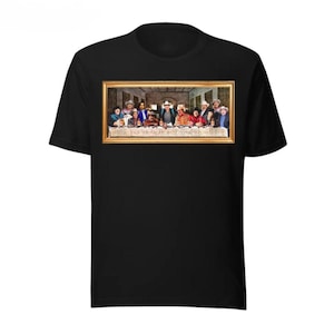 May include: Black t-shirt featuring a parody of The Last Supper painting. The artwork depicts a group of people in hats and casual attire seated at a table. The image is framed in gold.