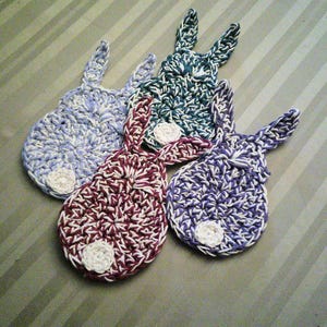 May include: Four crocheted bunny-shaped coasters in purple, blue, teal, and burgundy with white accents.