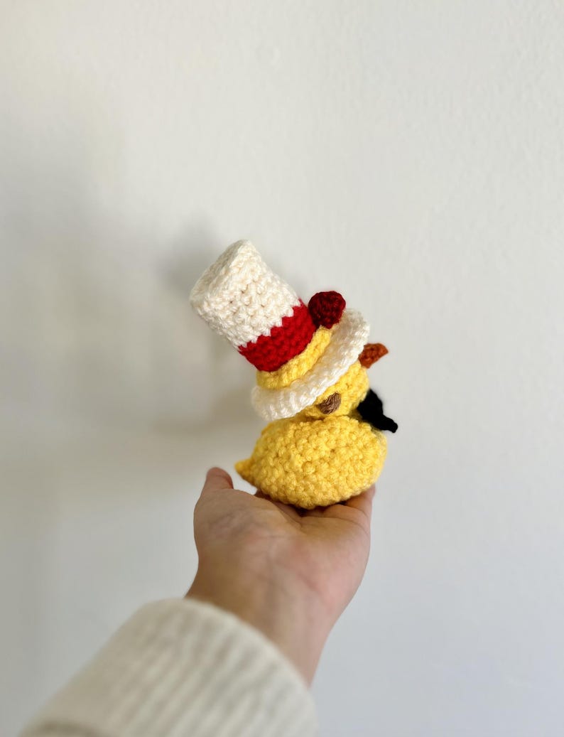 May include: A crocheted yellow chick wearing a red, white, and yellow hat with a red pom-pom.