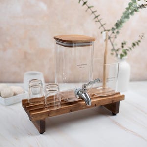 May include: A wooden stand with a glass dispenser labeled "Mouthwash" and two small glasses. The dispenser has a silver tap and a wooden lid.