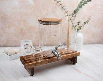 May include: A wooden countertop dispenser with a glass jar for mouthwash, a chrome faucet, and three glass cups. The dispenser is on a wooden stand with a bamboo lid.