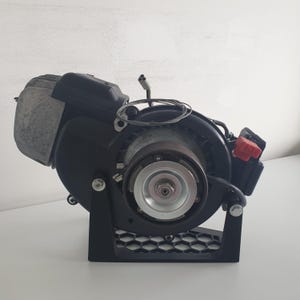 May include: A black and silver engine with a red switch, mounted on a black stand with a honeycomb pattern.