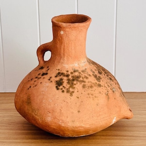 May include: A terracotta pottery vase with a handle and a spout. The vase has a mottled brown and green glaze.