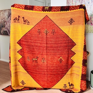 May include: A large, rectangular blanket in shades of yellow, orange, and red. The blanket showcases geometric patterns and stylized animal and tree motifs. A large diamond shape forms the central design, adding visual interest to the textile.