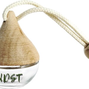 May include: A clear glass air freshener with a wooden top and a cream-colored string. The word "NOST" is printed in green on the glass. The wooden top is a light brown color. The string has a wooden bead.
