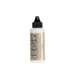 May include: A white bottle of Iron Orchid Designs erasable liquid chalk. The bottle has a black cap and a label with the brand name and product details. The label has a decorative design. The bottle contains 2 fl oz of white chalk.