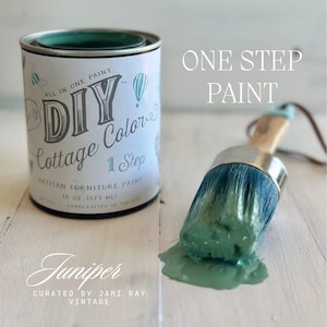 May include: A 16 ounce (475 ml) jar of green "DIY Cottage Colors" one-step artisan furniture paint in the color "Juniper". The jar has a white label with a whimsical design and the text "All in One Paint". A paintbrush with green paint on it is in the foreground.