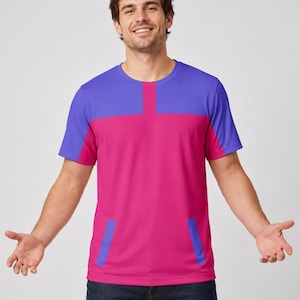 Pode incluir: Uma t-shirt de manga curta com gola redonda e design de blocos de cor. A parte superior do peito e as mangas são roxas, enquanto o corpo principal é cor-de-rosa brilhante. Dois detalhes retangulares roxos estão posicionados perto da bainha.