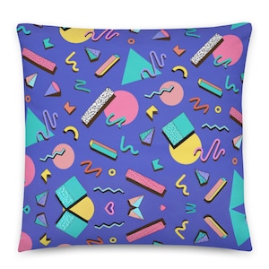 Könnte beinhalten: Ein quadratisches Dekokissen mit einem leuchtend violetten Hintergrund und einem sich wiederholenden Muster aus geometrischen Formen, darunter rosa Kreise, türkisfarbene Dreiecke, gelbe Halbkreise sowie verschiedene geschlängelte Linien und gesprenkelte rechteckige Balken.