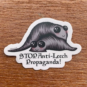 Puede incluir: Una pegatina con dos sanguijuelas de dibujos animados con grandes ojos expresivos y mejillas rosadas. Las sanguijuelas son grises con un aspecto texturizado. Incluye el texto "STOP Anti-Leech Propaganda!" en una fuente decorativa.