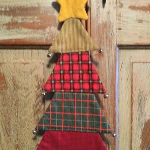 Könnte beinhalten: Ein Weihnachtsbaumschmuck aus Stoff mit einem gelben Stern. Der Baum besteht aus geschichteten Dreiecken aus verschiedenen karierten und roten Stoffen. Jedes Dreieck hat an jeder Spitze eine kleine silberne Glocke.