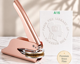 May include: A rose gold metal embosser with a lever handle and circular plates. Beside it is a white rectangular card featuring the green text A16 and an embossed circular design with the text FROM THE LIBRARY OF RHIANNON HICK.