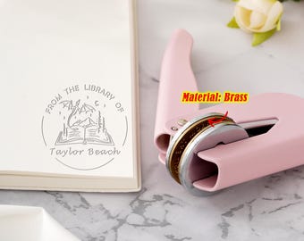 May include: A pink self-inking stamp with a brass stamp head. The stamp design features a dragon flying over an open book with the text "From the Library of Taylor Beach".
