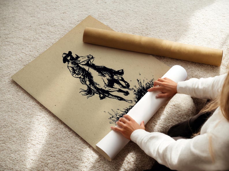 May include: A large square sheet of tan paper featuring a black ink illustration of a person riding a horse. The artwork depicts the rider and horse in motion, with textured lines and dark shading. A brown cardboard tube lies nearby on the surface.