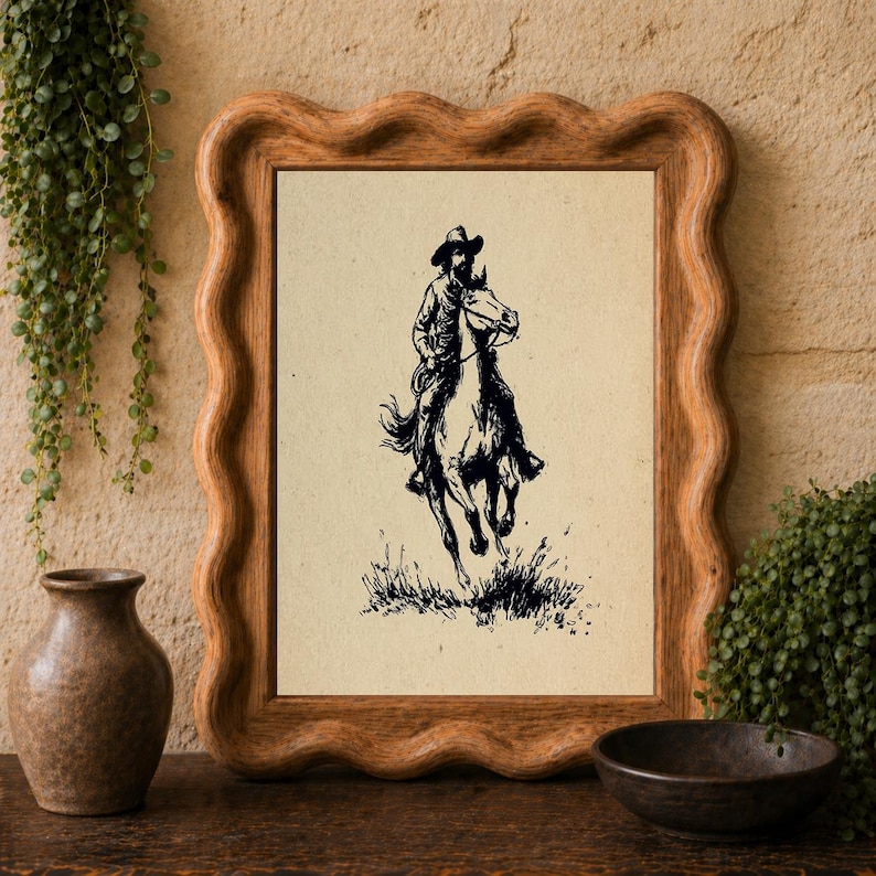 May include: A framed wall art piece featuring a black ink illustration of a cowboy riding a horse on a light beige background. The rectangular frame is made of light brown wood and has a distinct wavy, scalloped edge design.