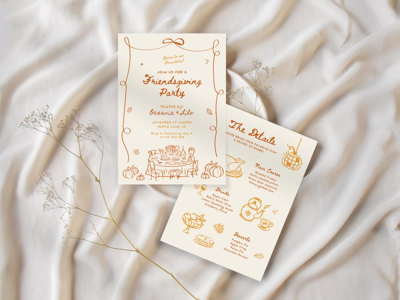May include: Two cream-colored Friendsgiving party invitations with orange illustrations and text. One card reads "Join us for a Friendsgiving Party" and the other lists the menu. The cards are on a white fabric background.