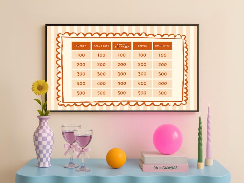 Op de afbeelding: Een ingelijst trivia-spelbord met categorie&euml;n en puntwaarden. Een vaas met een zonnebloem, twee wijnglazen met roze strikken, een roze ballon, een oranje bol, twee boeken en twee kaarsen staan op een blauwe tafel.